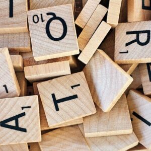 Ein Stapel verstreuter hölzerner Scrabble-Spielsteine mit schwarzen Buchstaben und Zahlen.